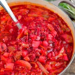 borscht soup in a stock pot with a metal ladle scooping some of the soup out.