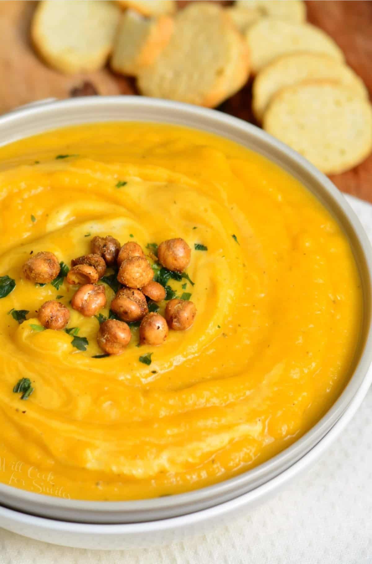 butternut squash in a bowl with chickpeas on top and bread slices in the background.