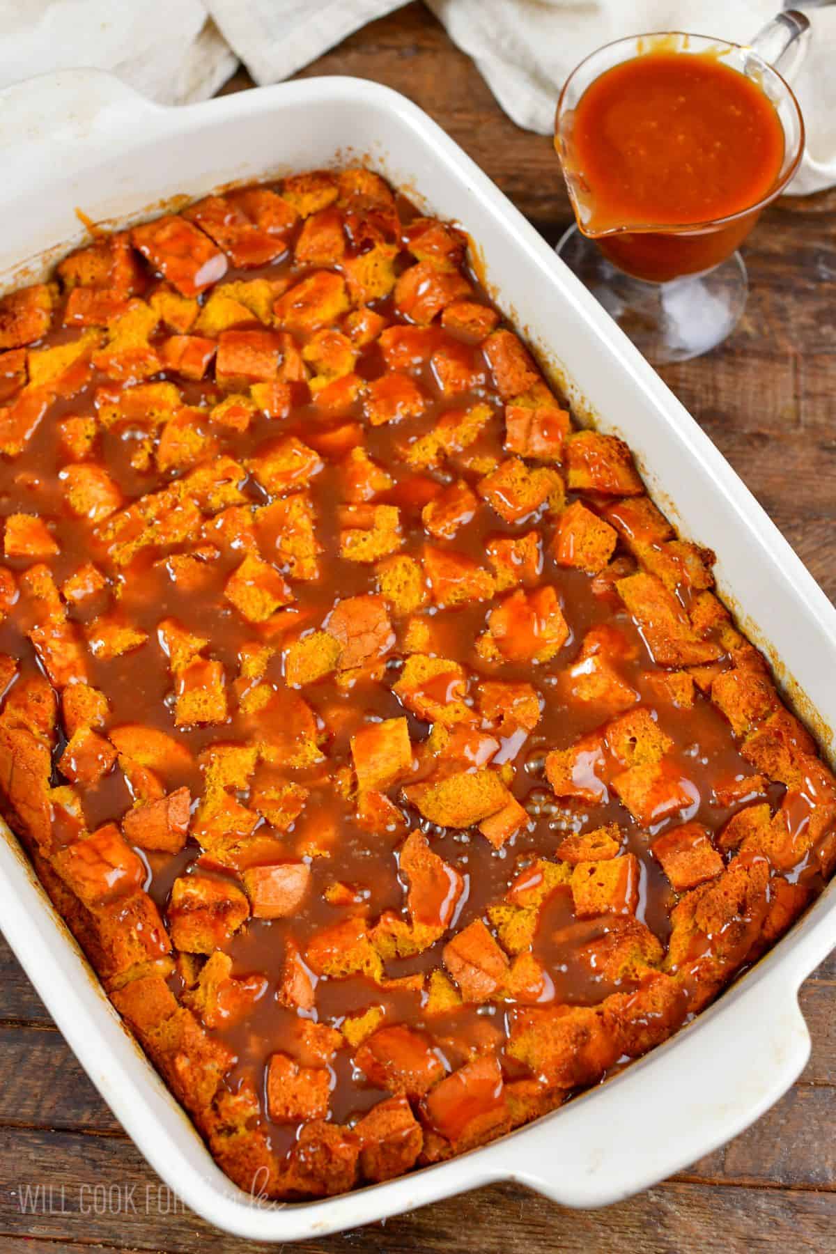 Pumpkin bread pudding with caramel over the top in a baking dish.