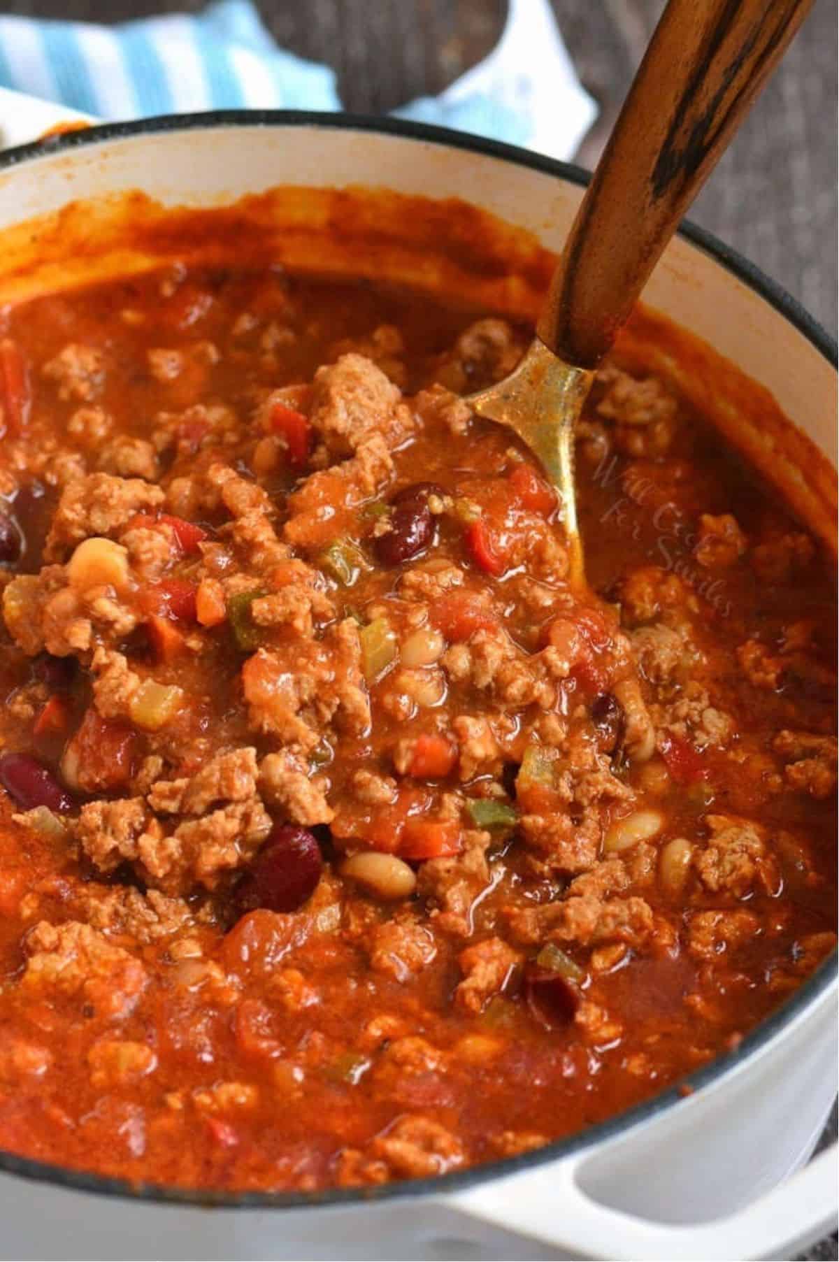 Chili in a Dutch oven pot with a spoon scooping the chili.