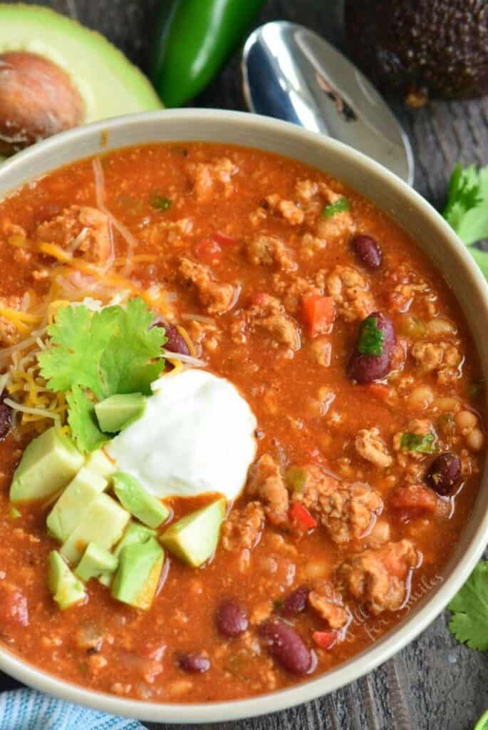 chili in a bowl with sour cream, avocado, and cilantro on a wood surface.