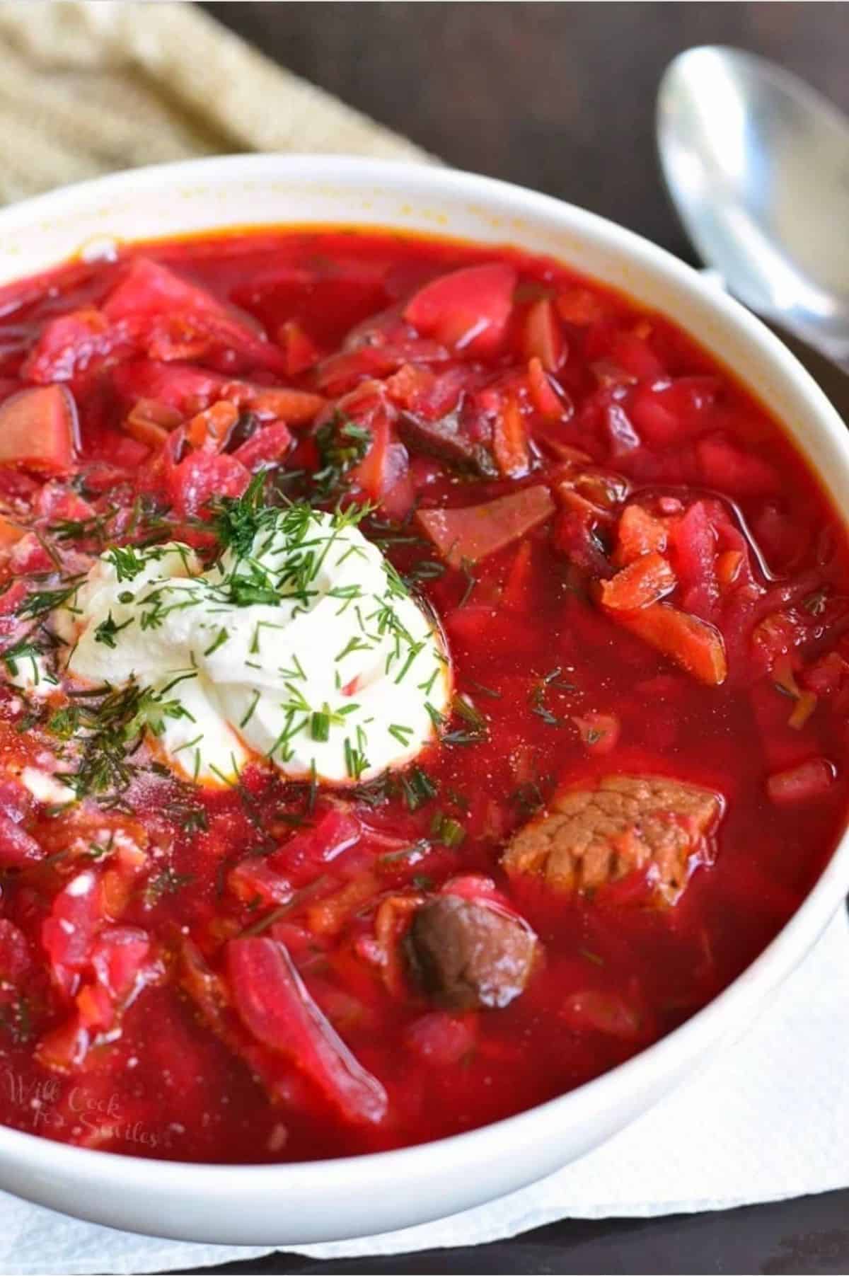 Borscht soup in a bowl with a dollop of sour cream on top and herbs as garnish.