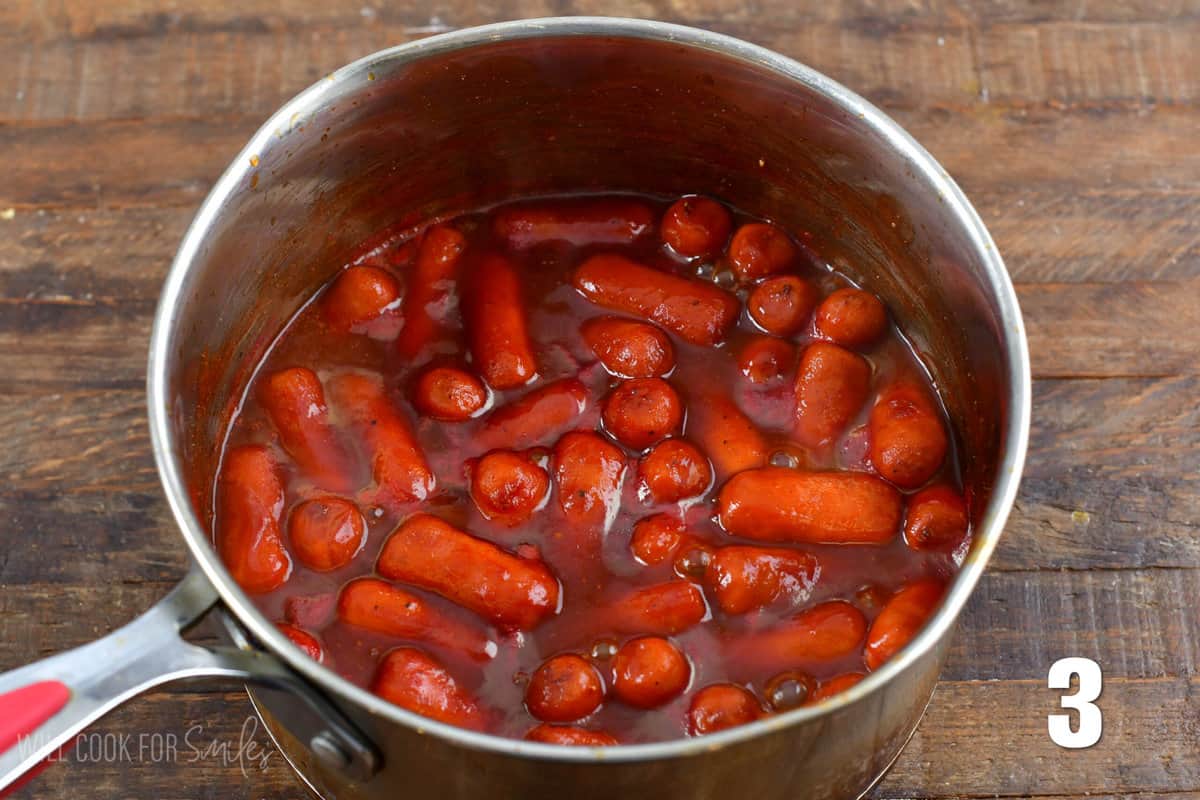 BBQ sauce and little smokies in a pot sitting on a wood surface.