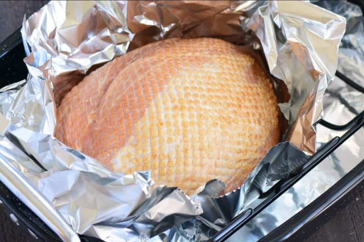 Uncooked ham in tin foil in a roasting pan.