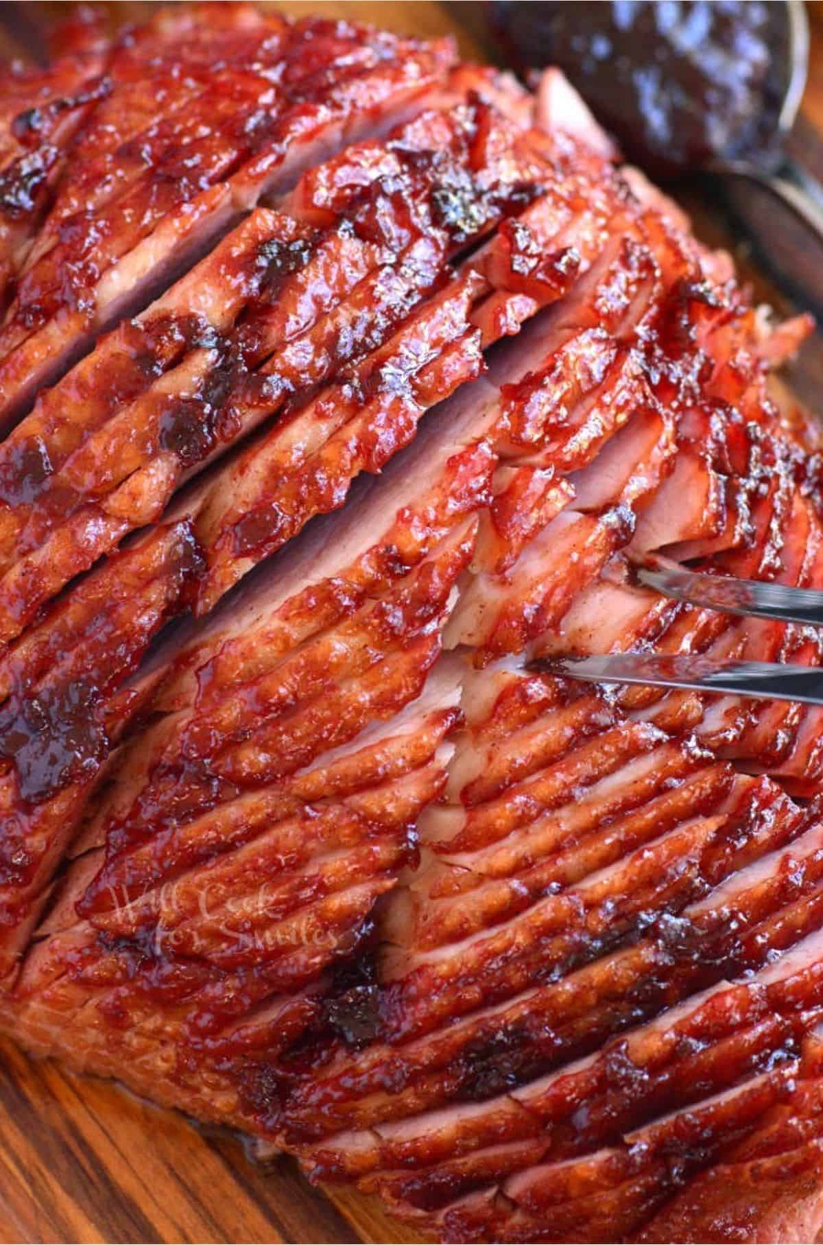 baked ham sliced on a cutting board with a big fork