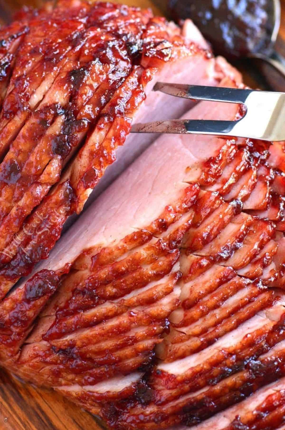 baked ham on a cutting board with a fork pulling the sliced pieces apart.