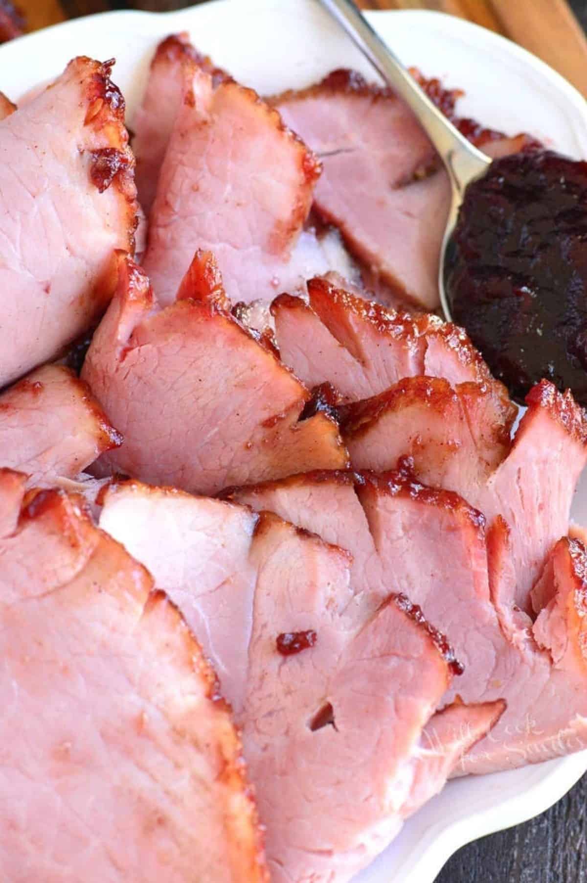 slices of baked ham on a plate with a spoon of cherry glaze.