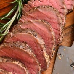 sliced beef tenderloin with seasoning on the sides and rosemary sprig next to it.