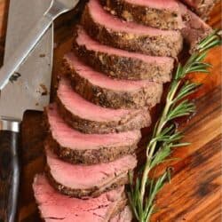 sliced beef tenderloin spread on cutting board next to a knife and rosemary.