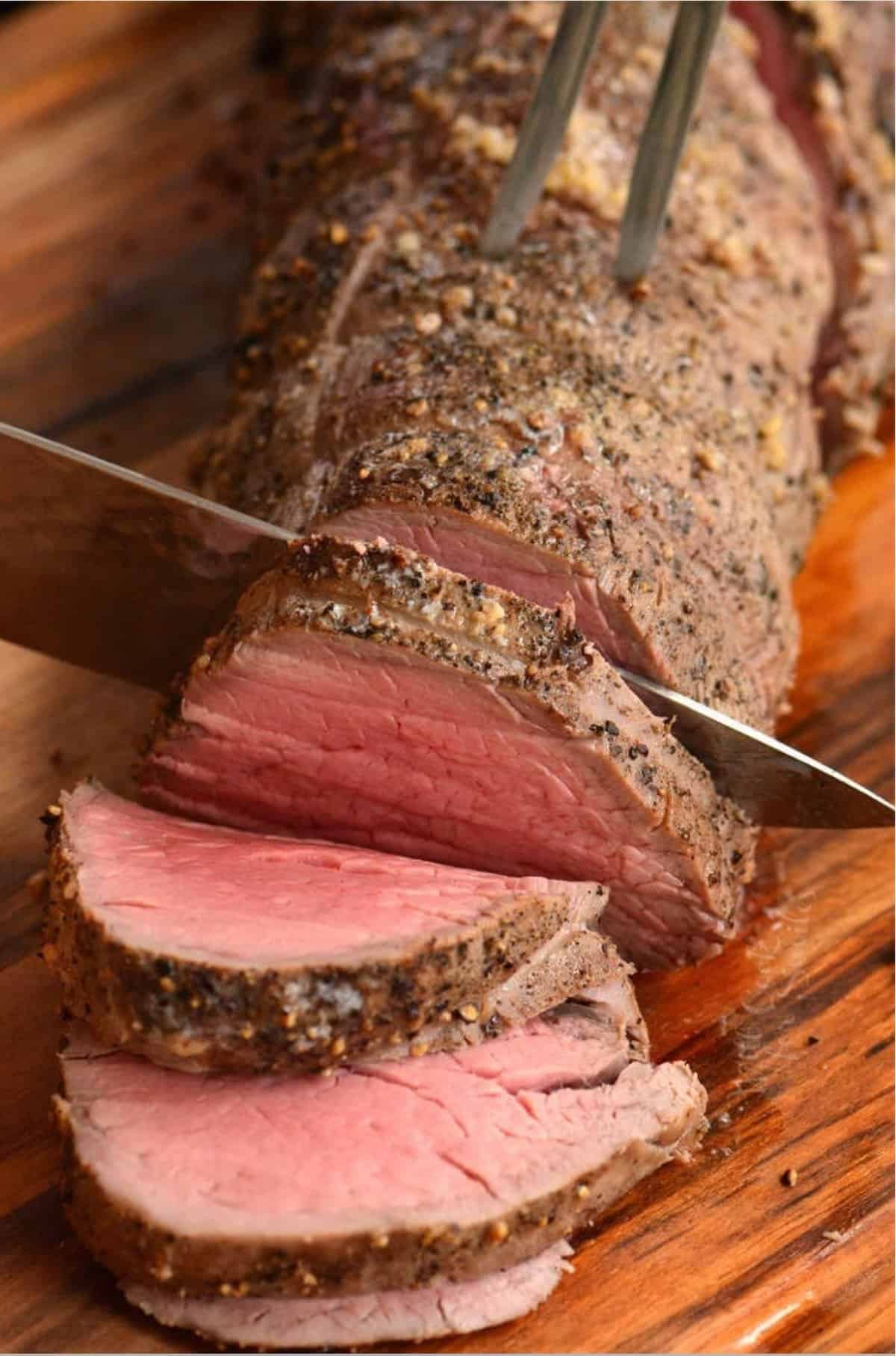 slicing through a beef tenderloin with a knife and a fork.