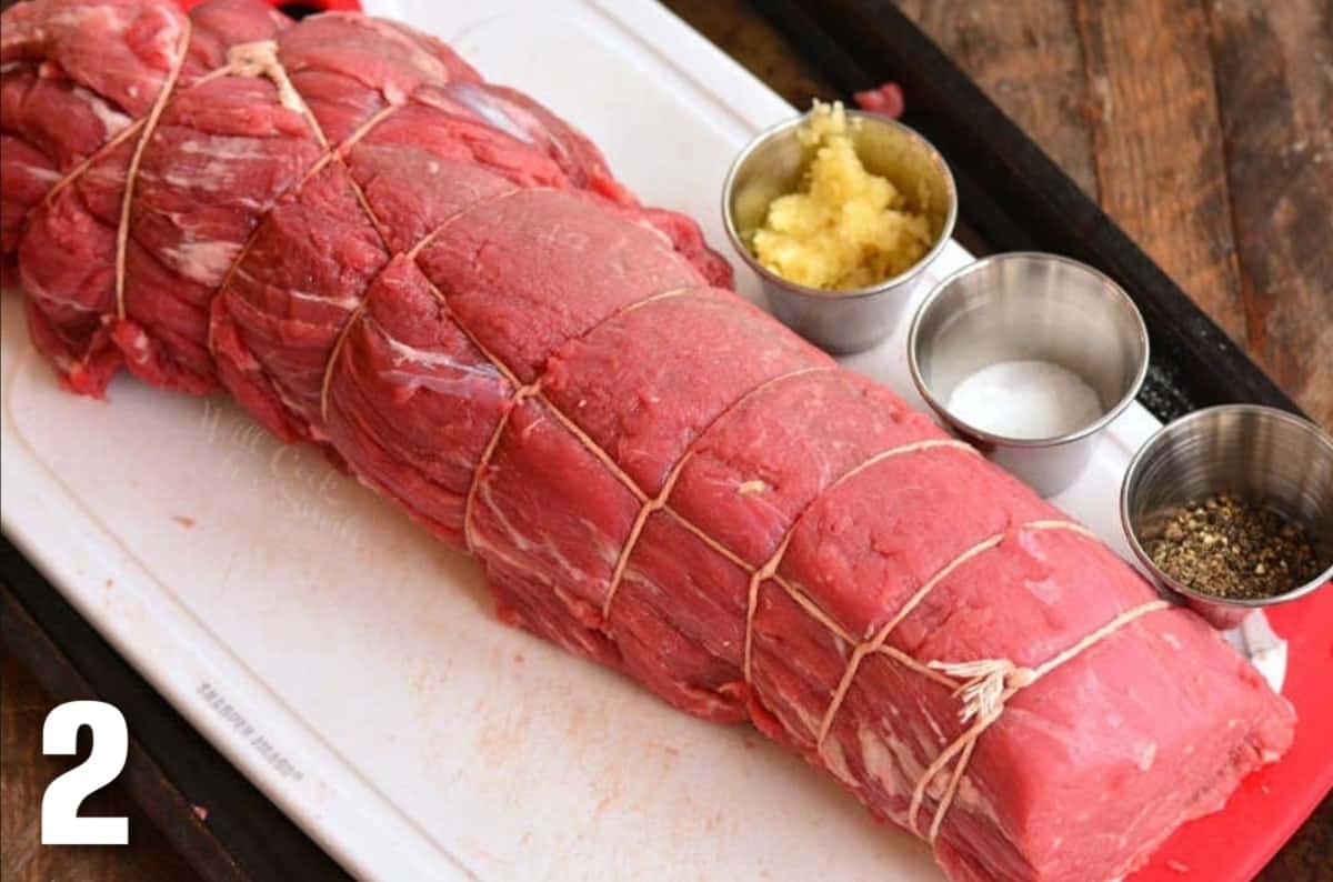 tied beef tenderloin next to pressed garlic, salt, and pepper.