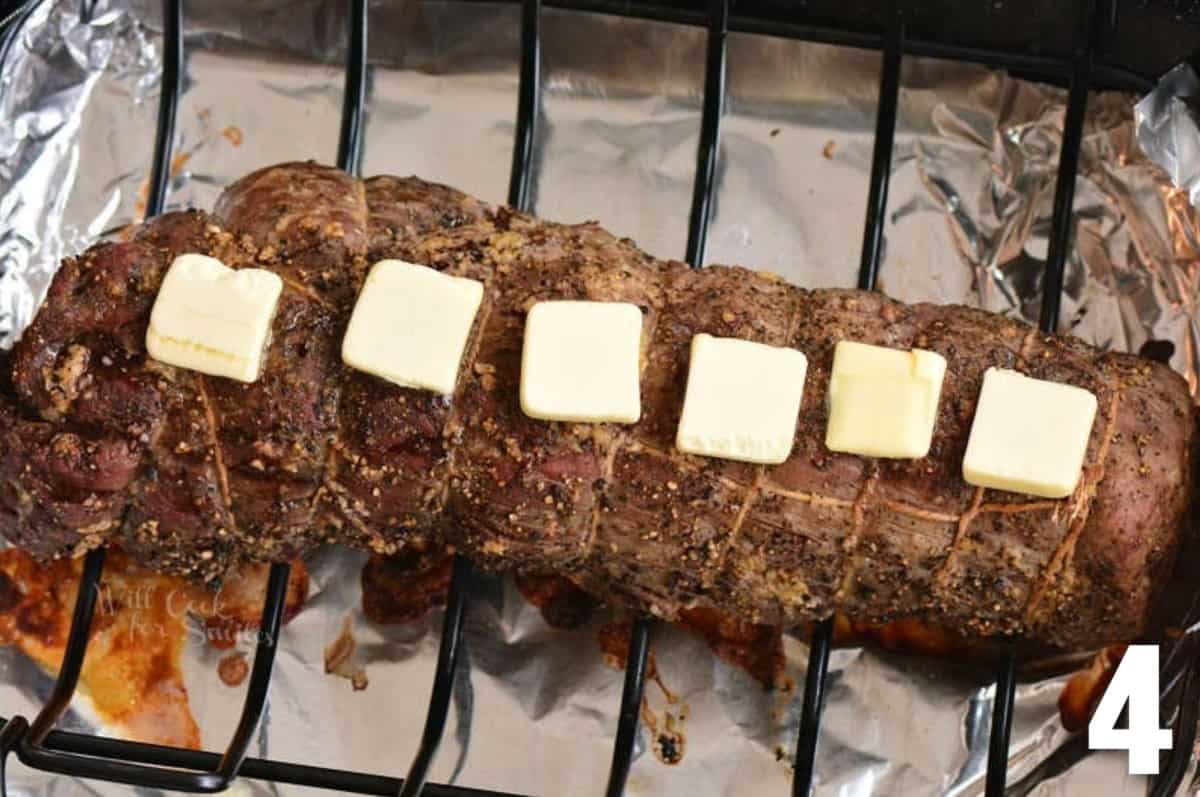 cooked and tied beef tenderloin with butter sliced on top.