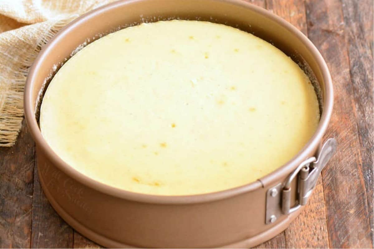 Baked cheesecake in a springform pan on a wood table.