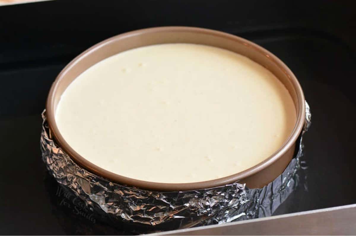 Eggnog cheesecake in a springform pan covered in tin foil.