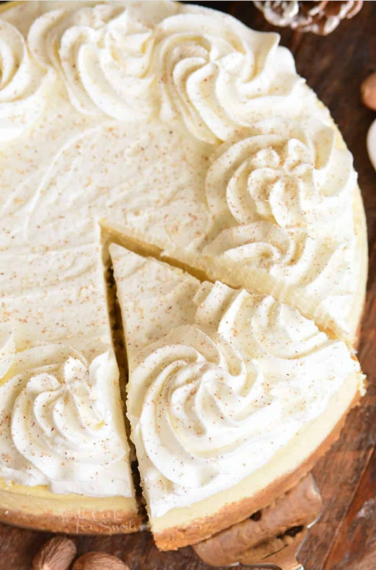 whole eggnog cheesecake with a slice on a wood surface.