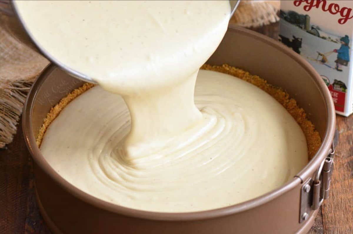 pouring batter into the springform pan on a wood table.