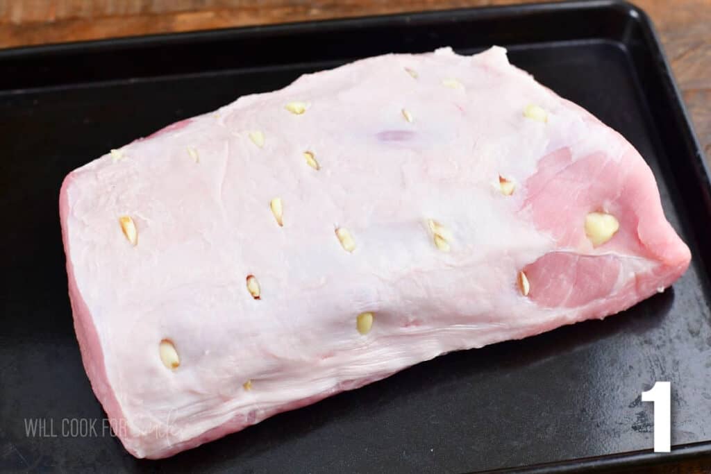 pork loin with garlic slices inserted into slits in the meat on the baking sheet.