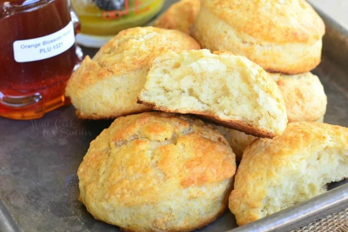 honey butter biscuits with on a baling sheet with one cut in half and honey also on the baking sheet.