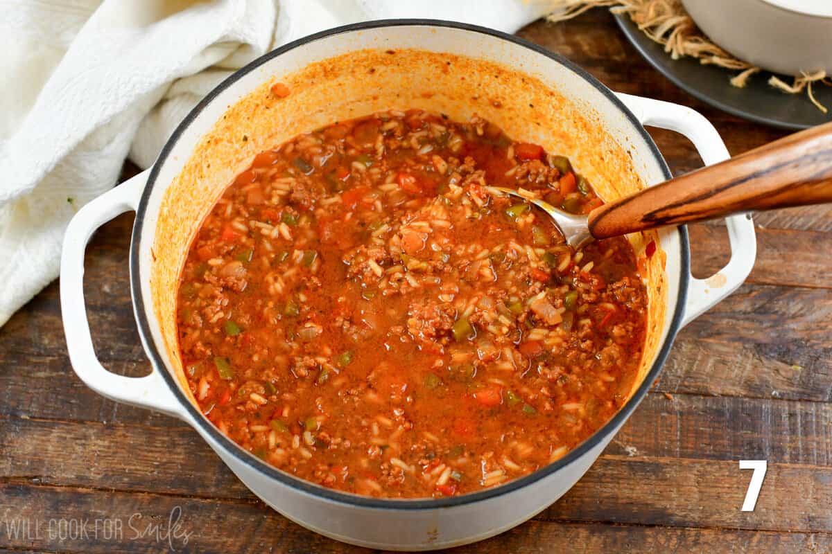 stuffed pepper soup in a pot on a wood table with a spoon inside the pot.