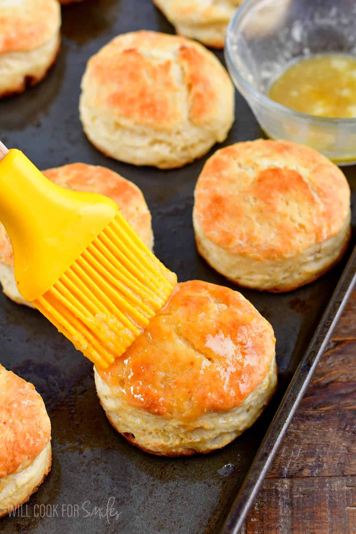 brushing honey butter on top of biscuits.