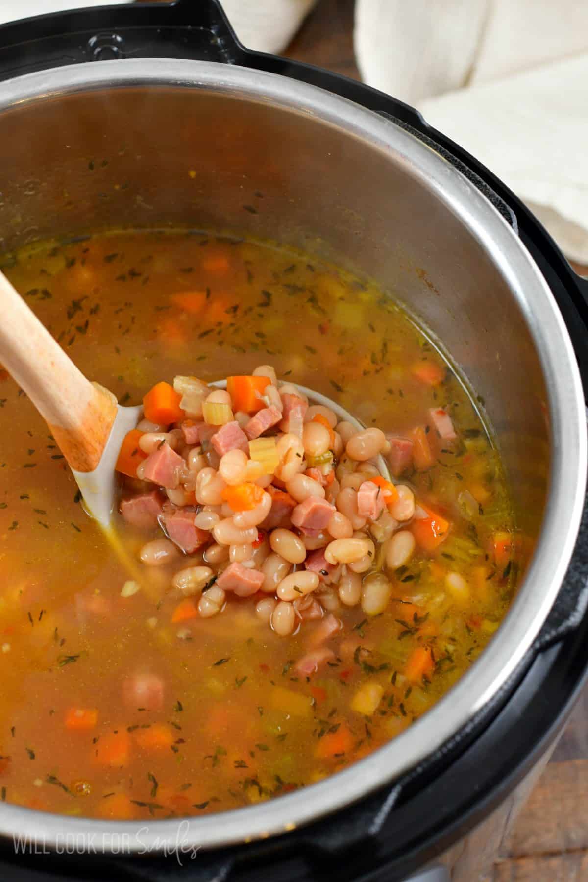 ham and bean soup in an instant pot with a wood ladle scooping some out.