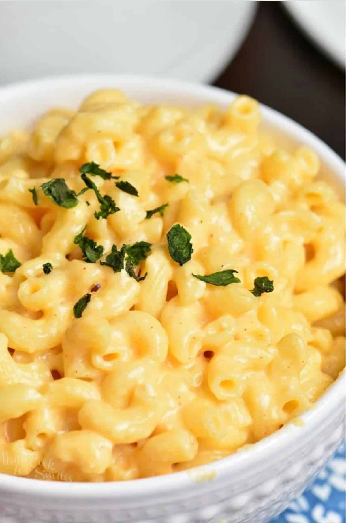 creamy cheesy macaroni in a white bowl topped with green parsley.
