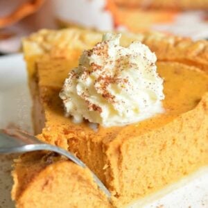 cutting through a slice of pumpkin pie topped with whipped cream with a fork.