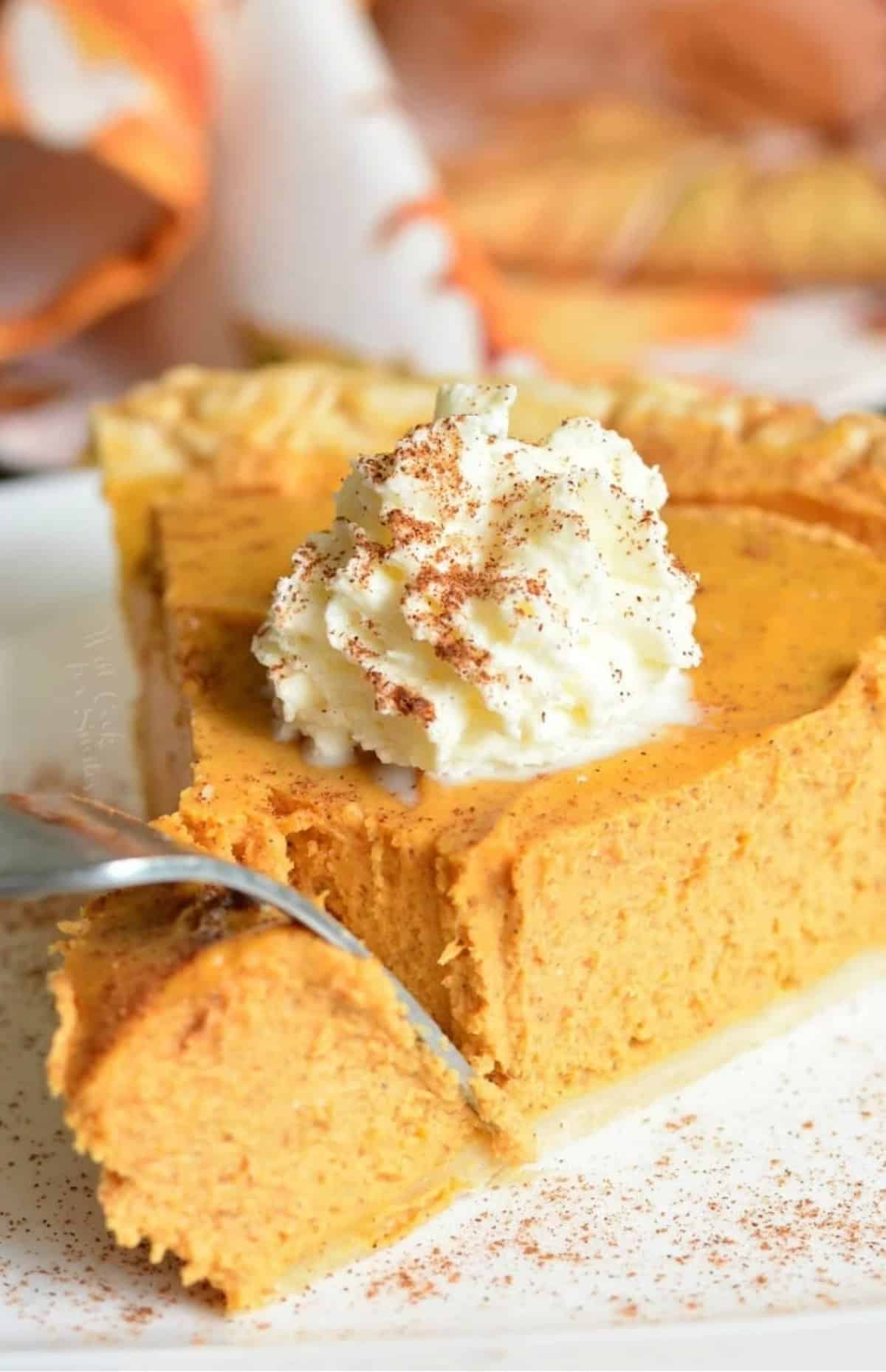 cutting through a slice of pumpkin pie topped with whipped cream with a fork.