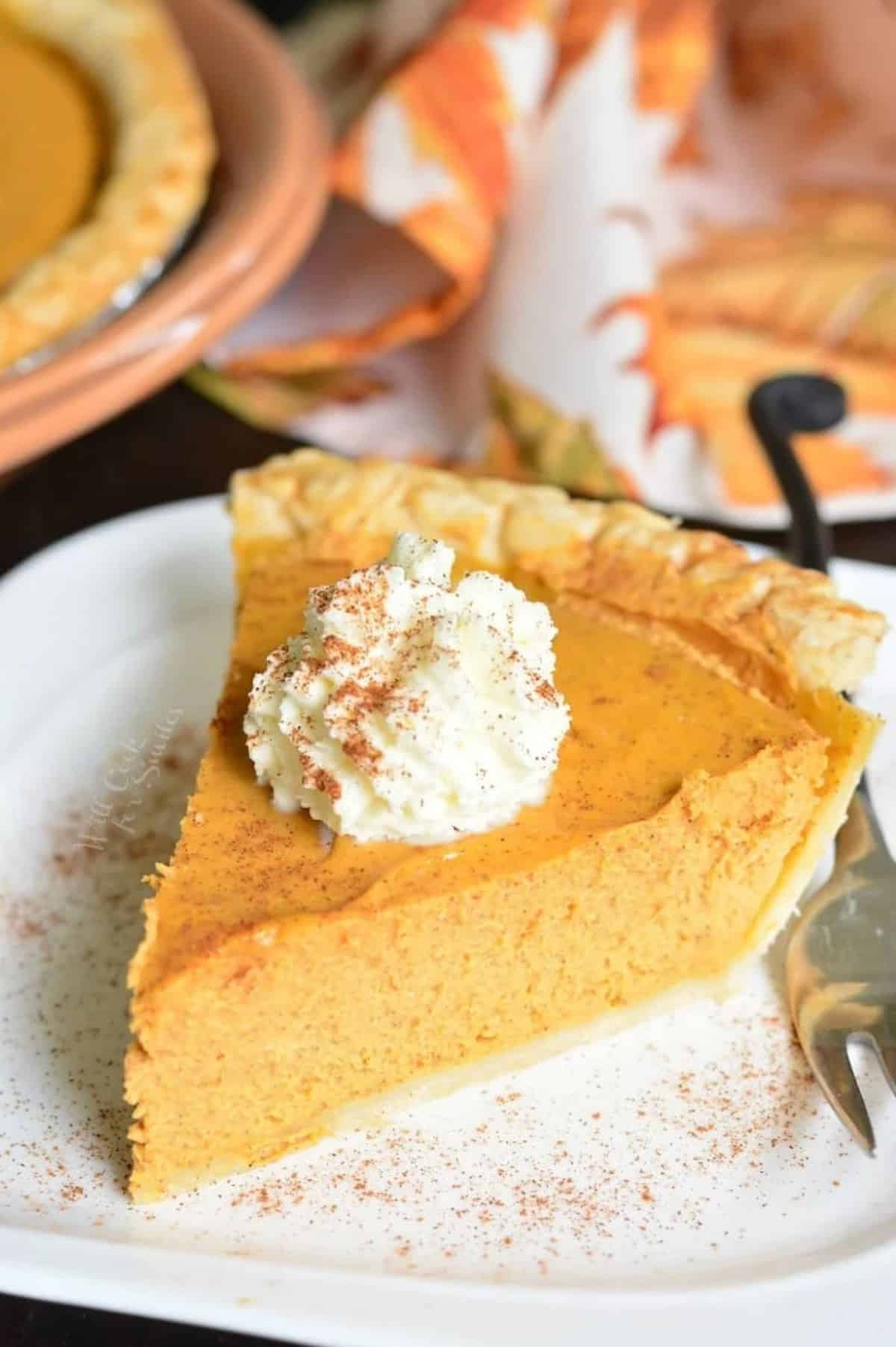 a slice of pumpkin cheesecake pie topped with whipped cream and cinnamon.