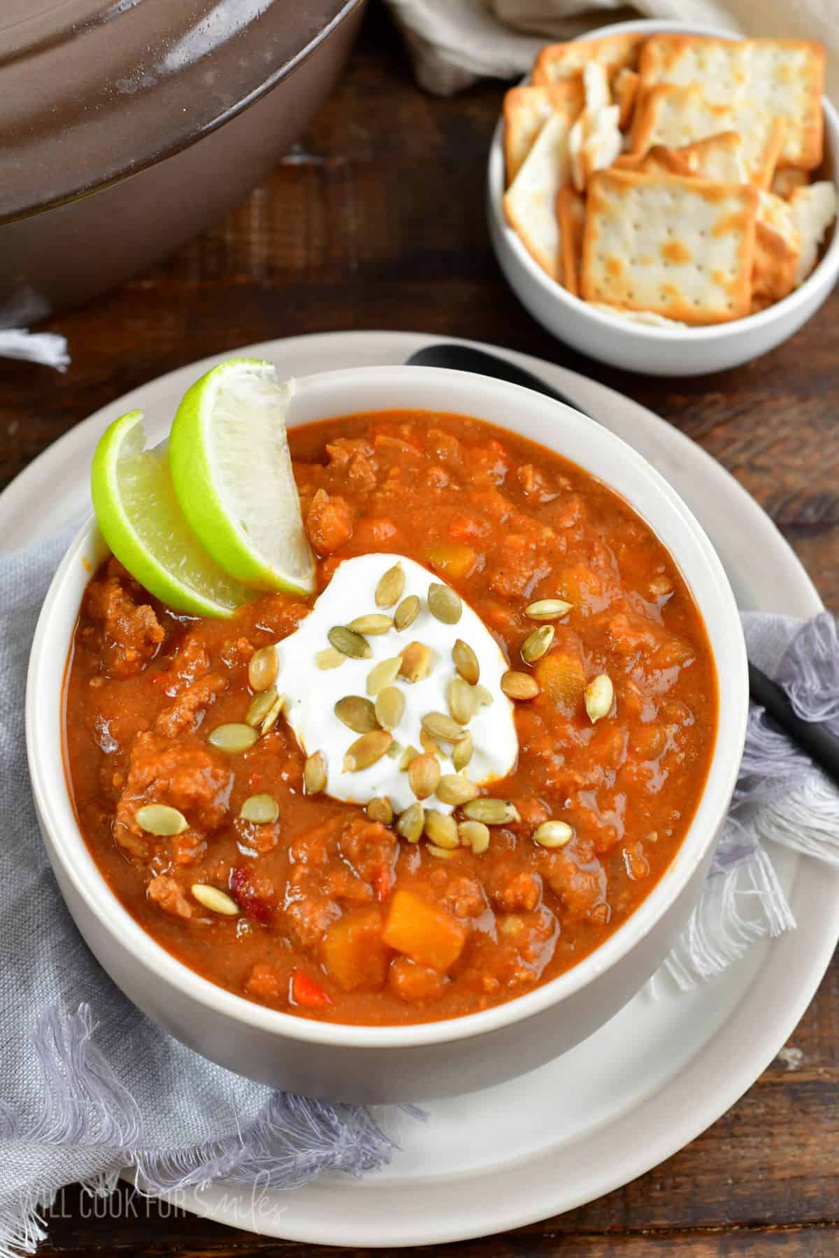 pumpkin chili in a bowl with a lime, sour cream, and pumpkin seeds as garnish on top.