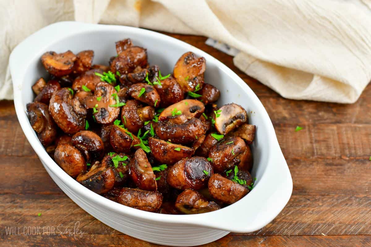 roasted mushrooms in a serving dish on a wood surface with a linen napkin.