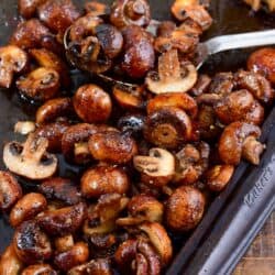 roasted mushrooms on a baking pan with a metal spoon on a wood surface.
