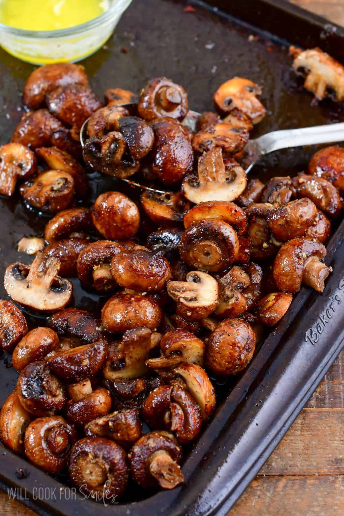 roasted mushrooms on a baking pan with a metal spoon on a wood surface.