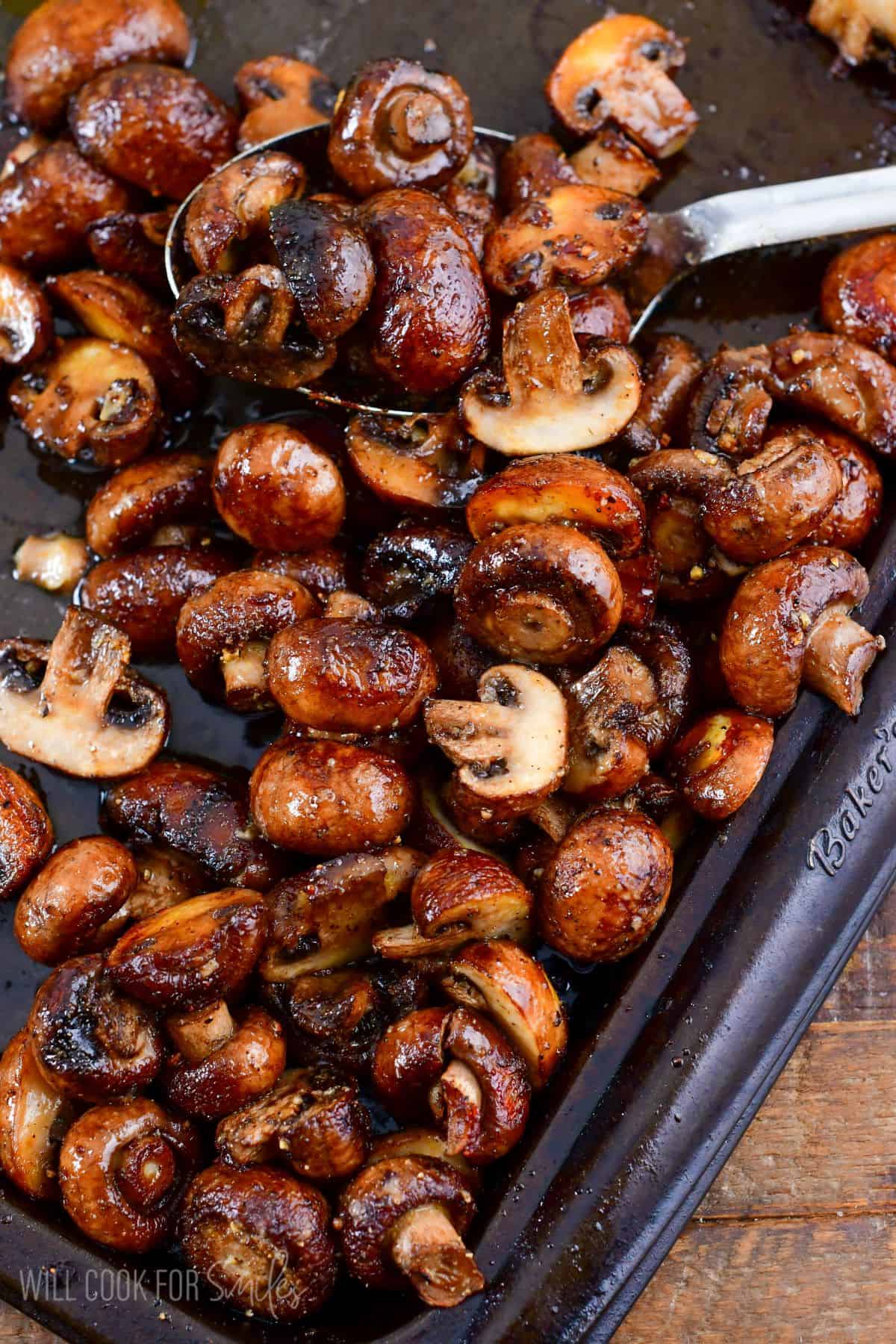 roasted mushrooms on a baking pan with a metal spoon.