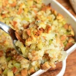 stuffing on a serving spoon with the rest in a casserole dish in the background.