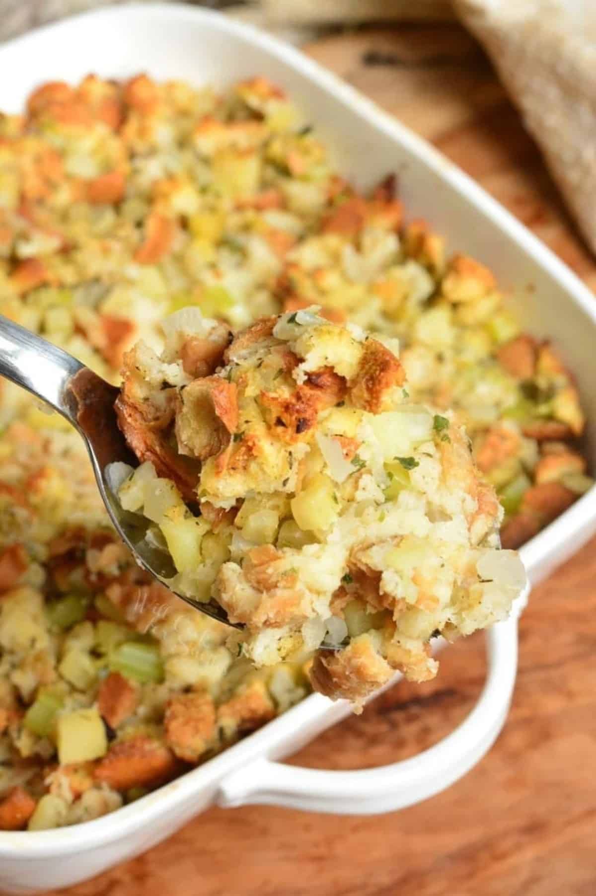 stuffing on a serving spoon with the rest in a casserole dish in the background.