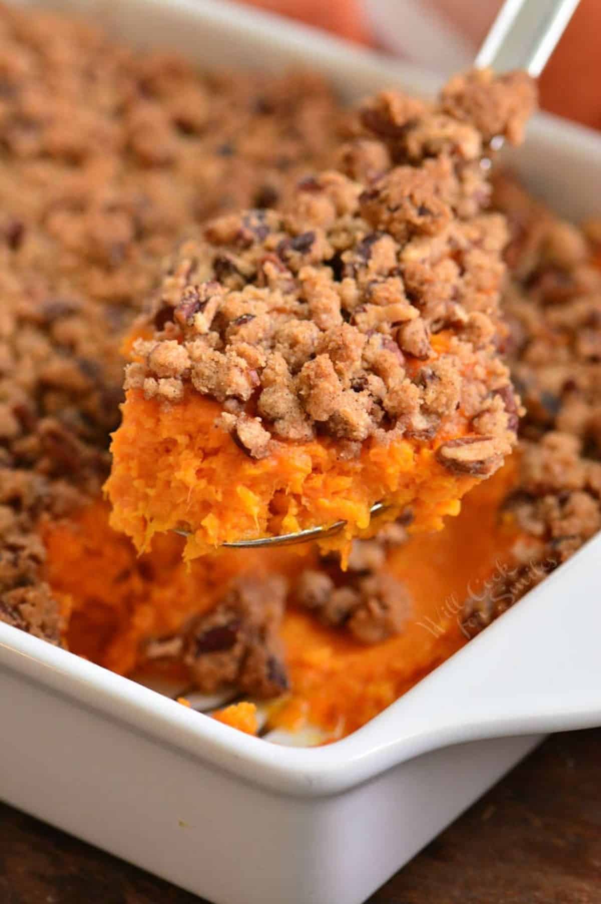 holding scooped sweet potato casserole on a silver spoon over the baking dish.