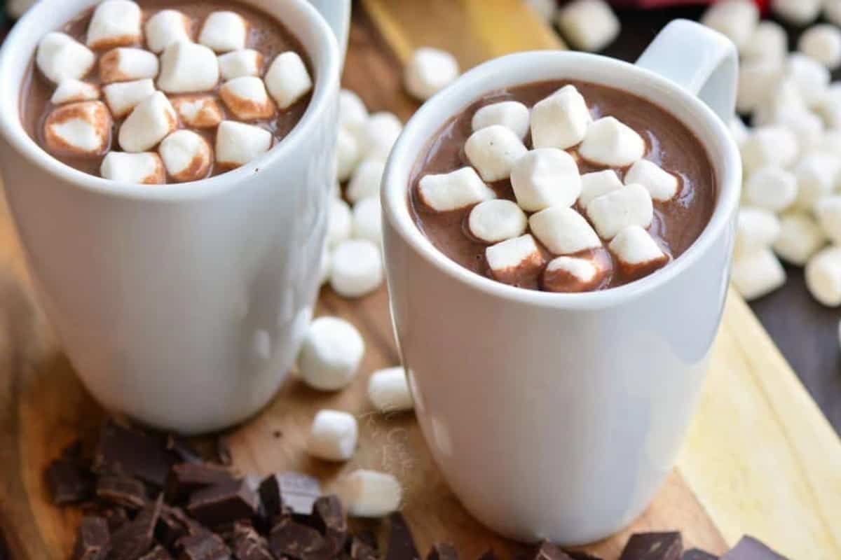 two mugs of hot chocolate on a wood cutting board.
