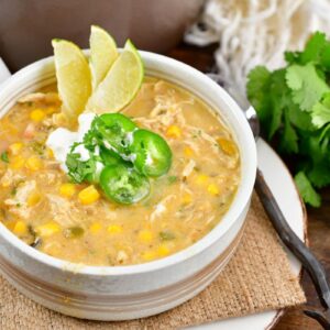 white chicken chili in a bowl with three sliced limes, jalapeno, and sour cream on top.