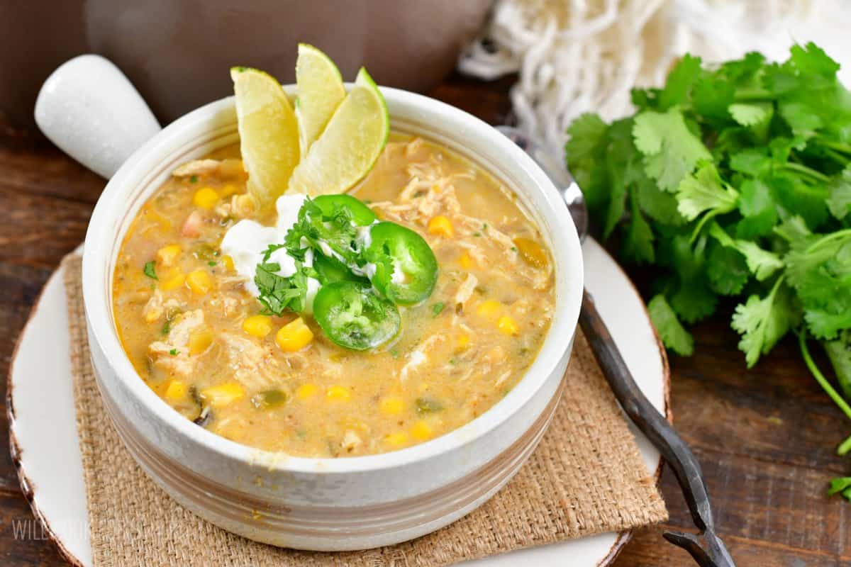 white chicken chili in a bowl with three sliced limes, jalapeno, and sour cream on top.