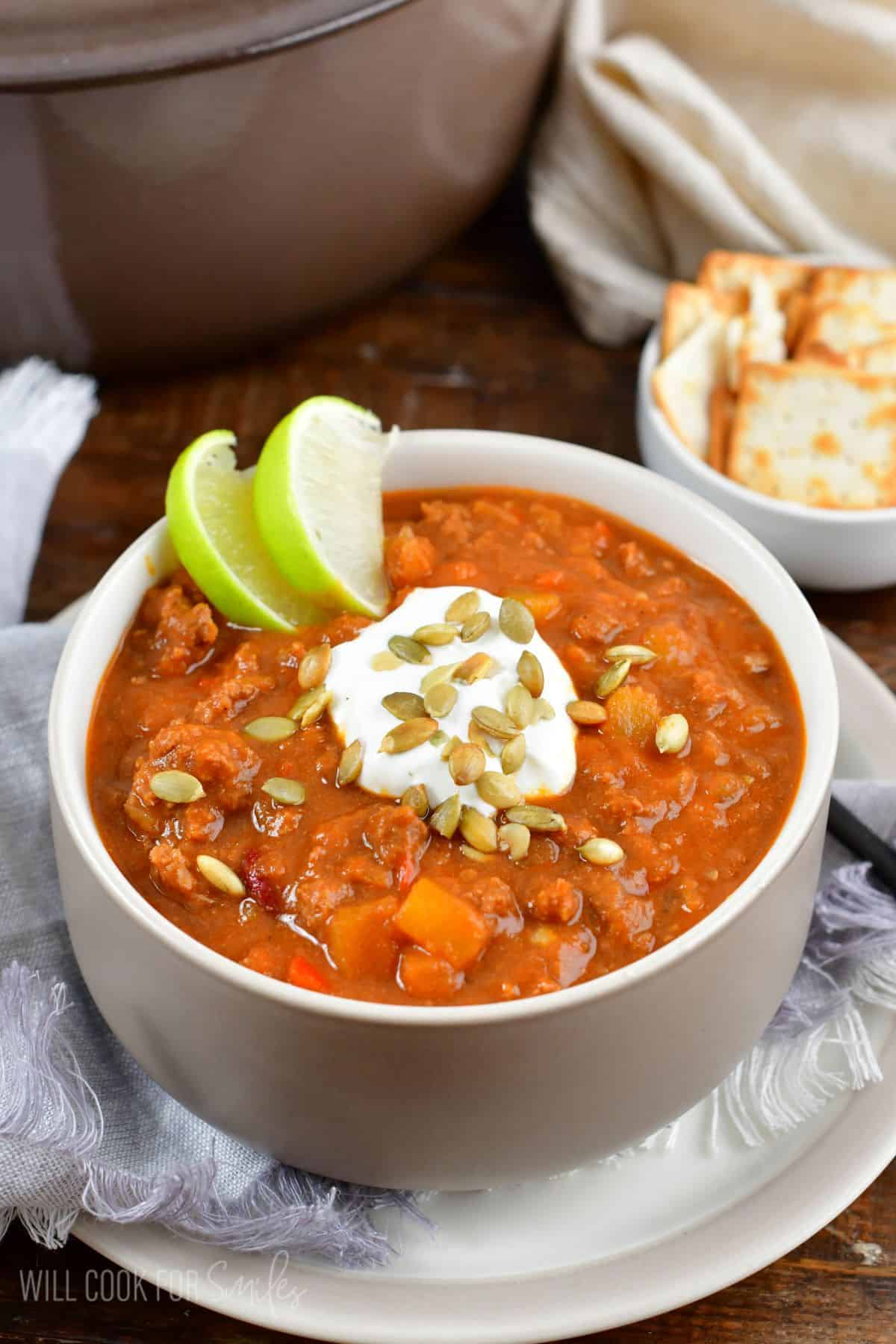 pumpkin chili in a bowl with a lime, sour cream, and pumpkin seeds as garnish on top on a plate.