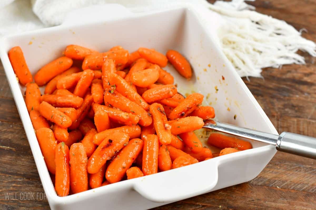 glazed balsamic roasted carrots in the white ceramic dish with a spoon.