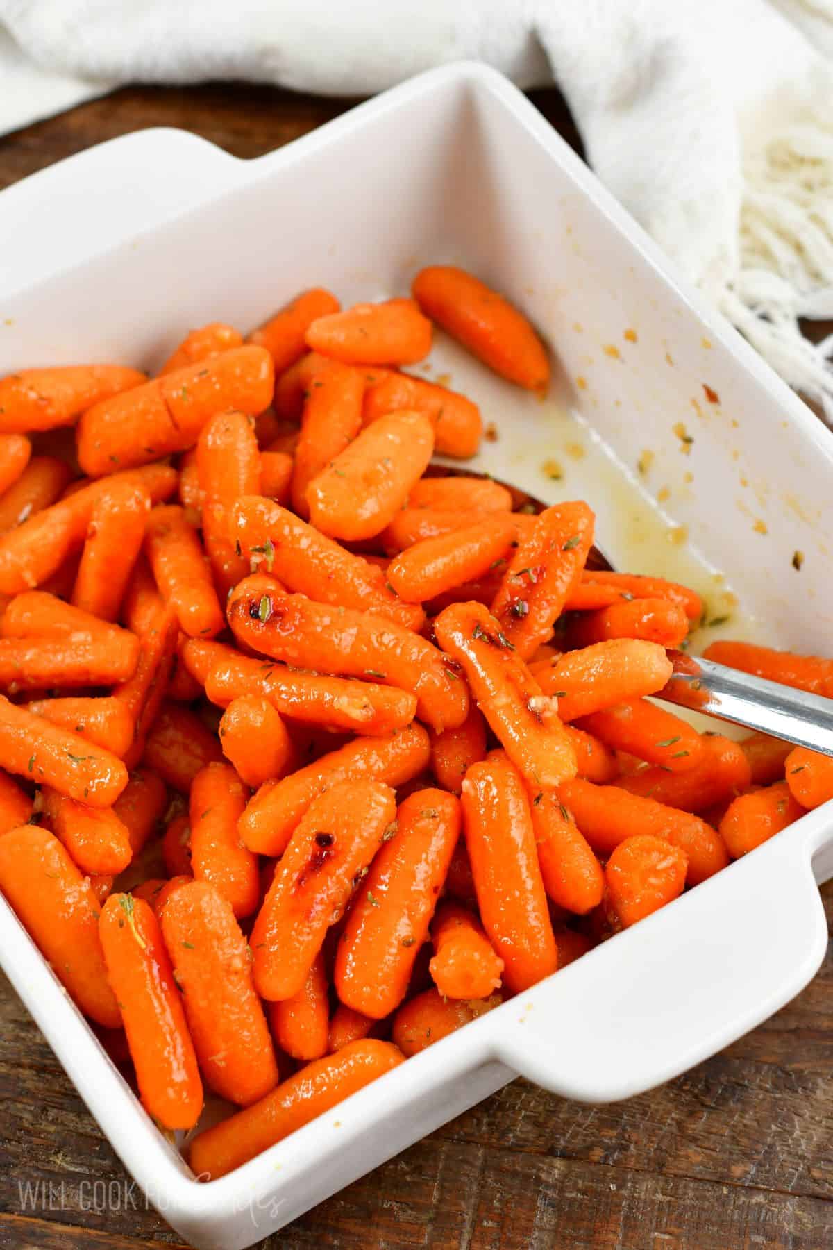 scooping some roasted carrots from a white dish.