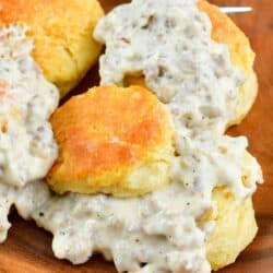 plate with several biscuits with sausage gravy over them on a wood plate.