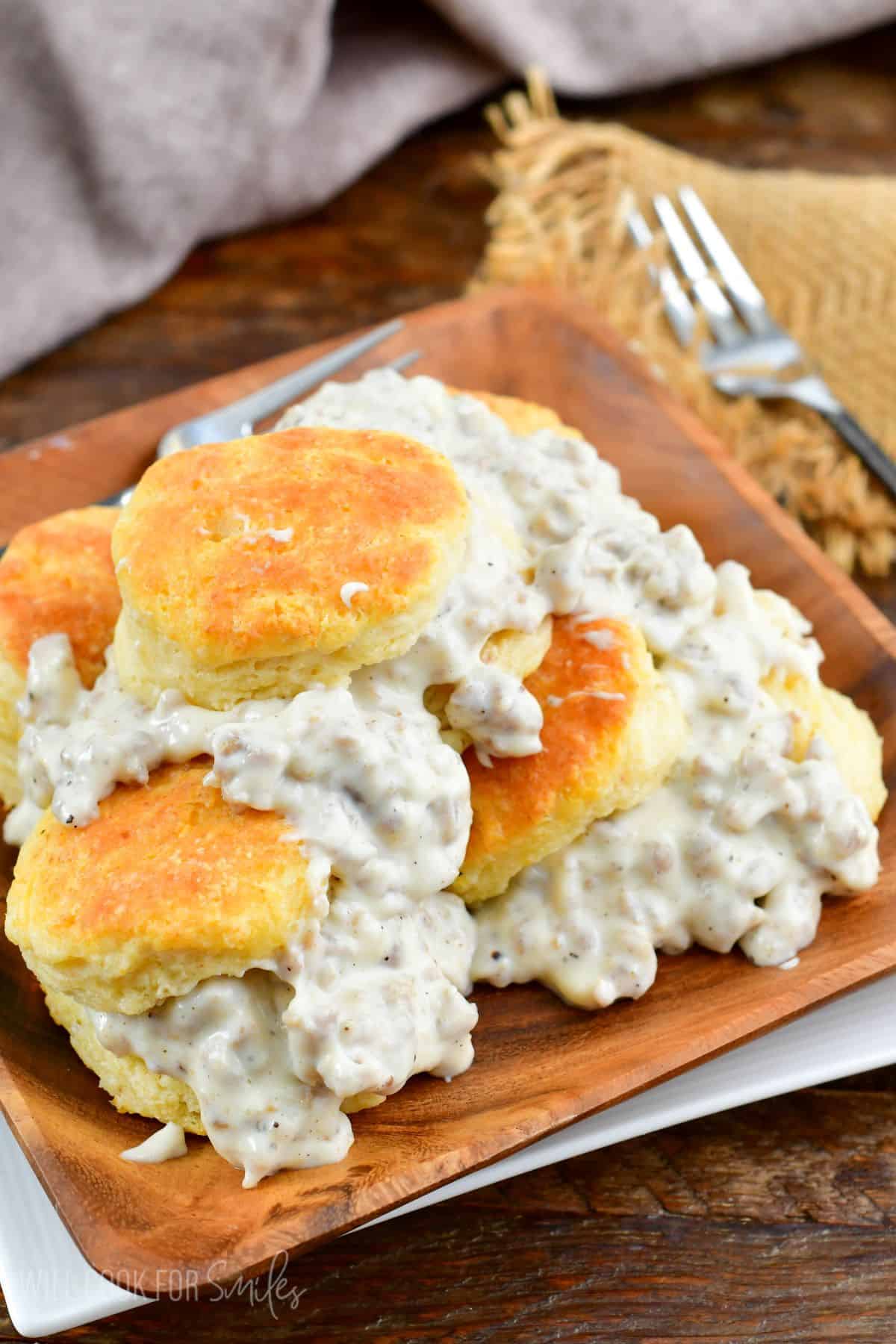 biscuits stacked up with sausage gravy over them on a wood plate.
