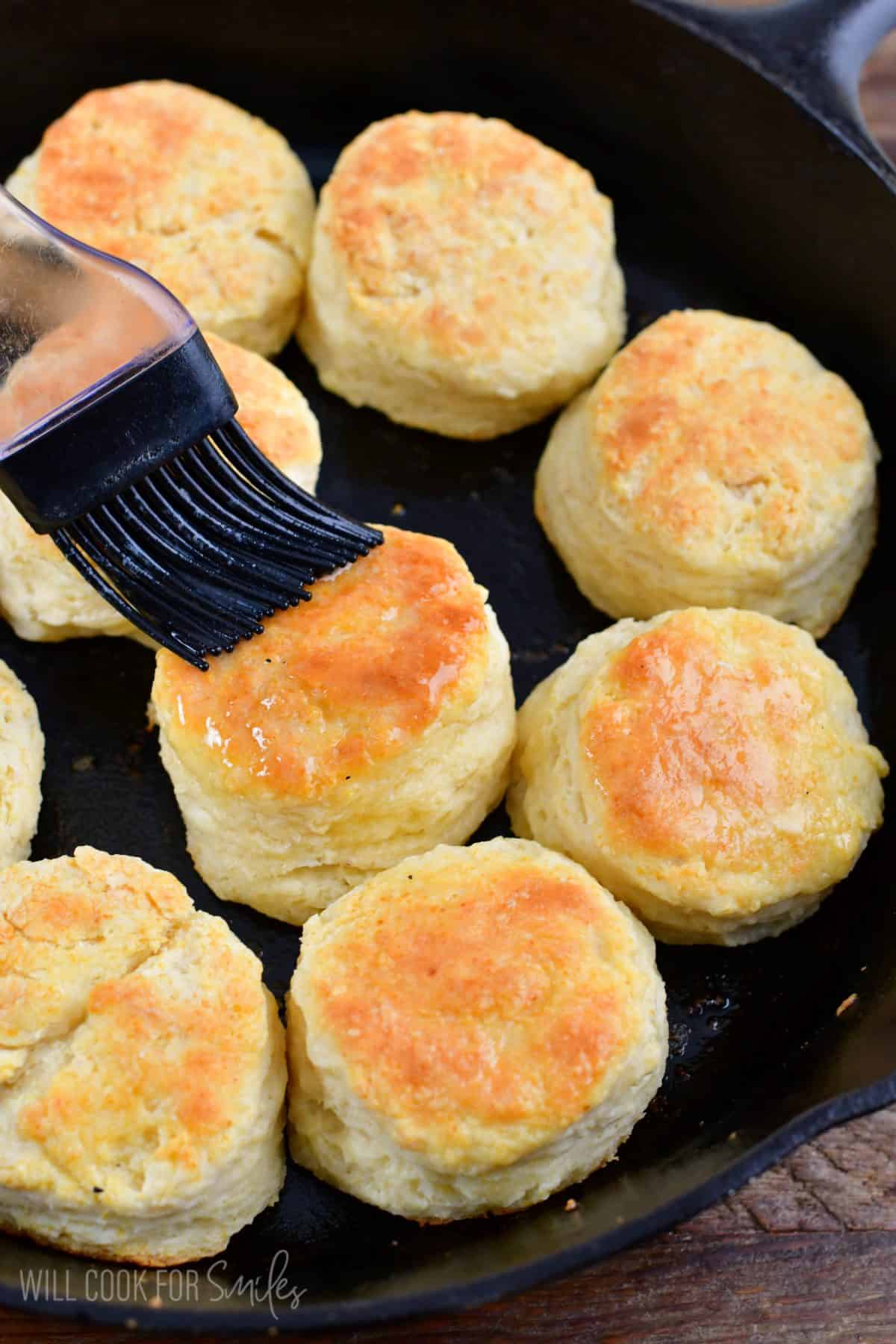 Brushing butter on cooked buttermilk biscuits in a skillet.