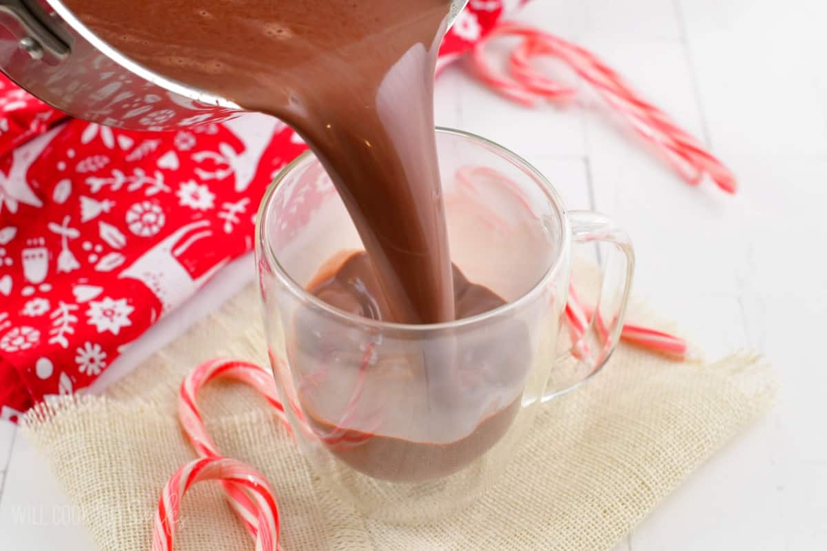 pouring peppermint hot chocolate into a glass with candy canes around.