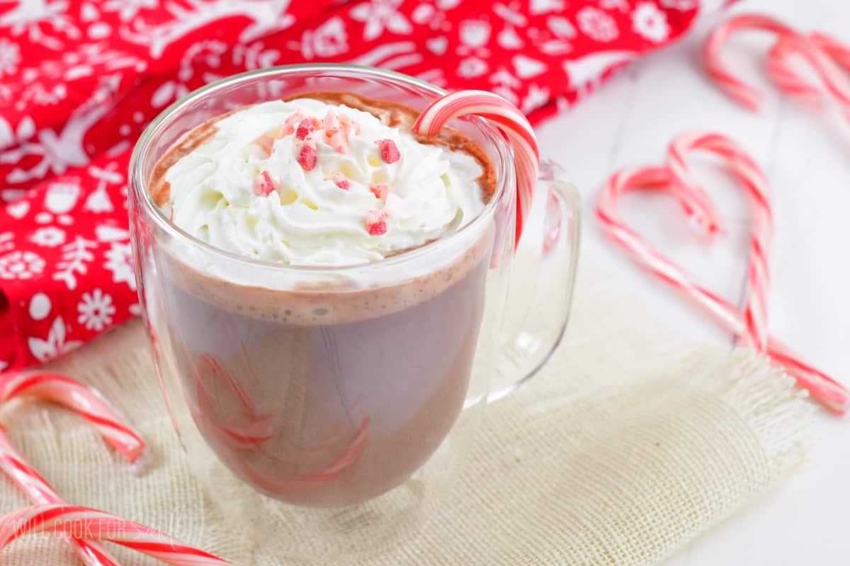 peppermint hot chocolate in a glass mug with whipped cream and peppermint crunch and candy canes.