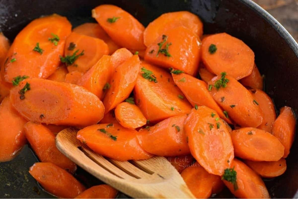 scooping glazed carrots from the pan with wooden spoon.