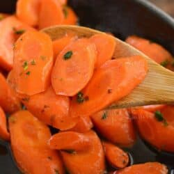 scooped honey glazed carrots on a wooden spoon over the skillet.